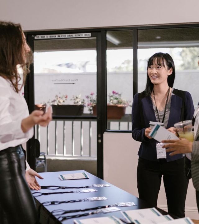 Businesswomen registering at a conference desk, smiling and interacting in a professional setting.